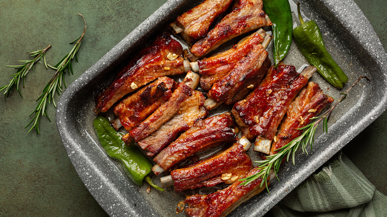 A layer of pork ribs in a baking pan with herbs and peppers