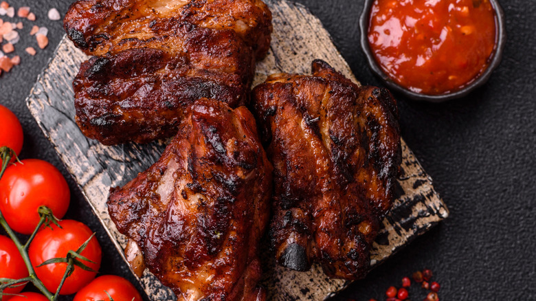 Several pork ribs with barbecue sauce on a wooden block next to a number of small tomatoes on the vine