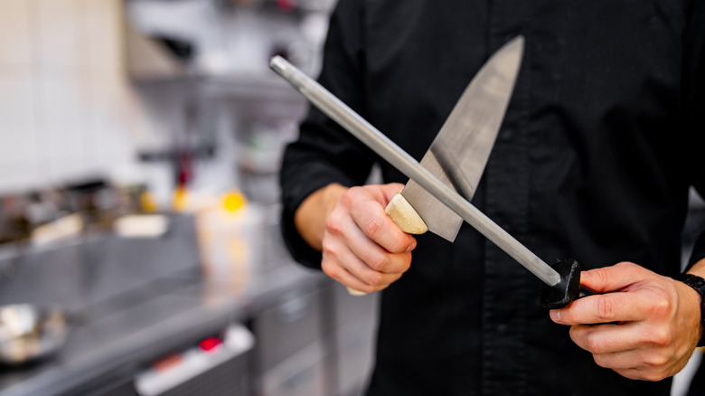 Person dressed in black holding chefs knife and honing rod