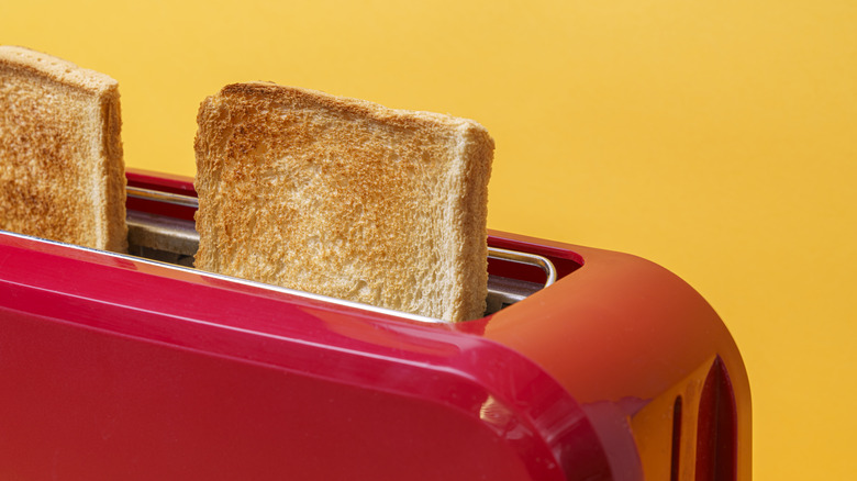 A red toaster with some toast, against a yellow background.