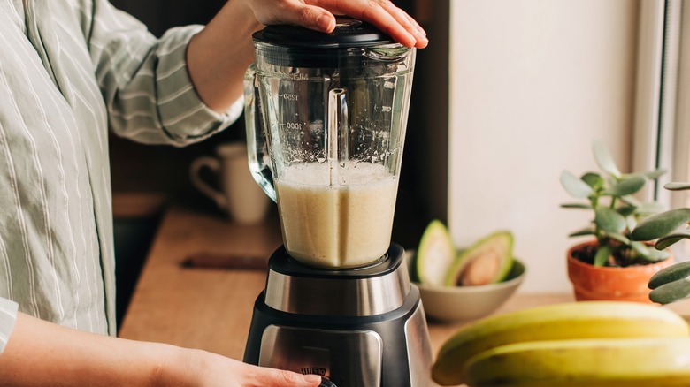 A person makes a smoothie in a blender on a kitchen counter