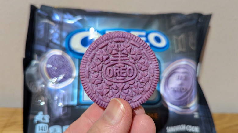 Hand holding purple BTS Oreo collab in front of Oreo package on kitchen counter.