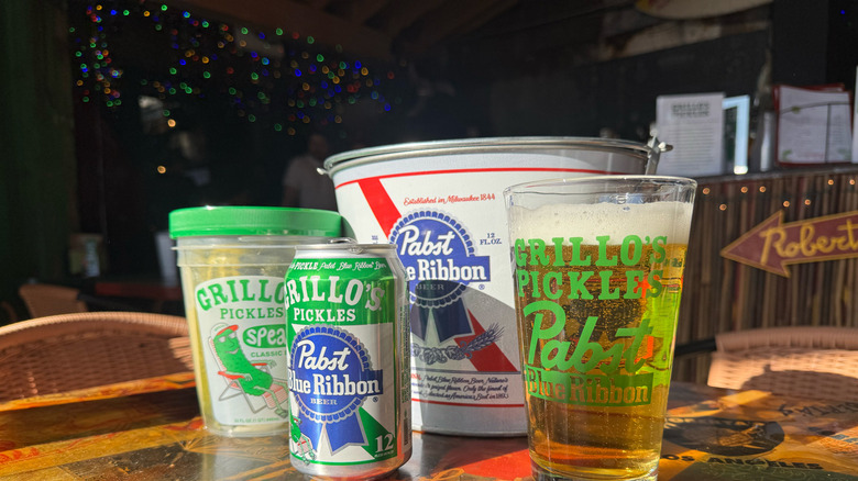 PBR x Grillo's Pickles pickle beer in glass and can in front of PBR bucket and jar of pickles