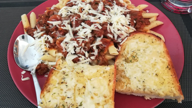 A plate of PastaBravo pasta, covered in sauce and cheese, with garlic bread.
