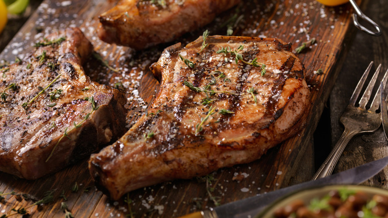 Pork chops with grill marks on cutting board with salt and herbs.