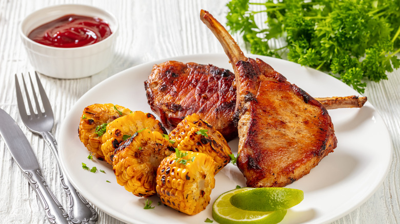Two pork chops on a plate with slices of corn on the cob on a farmhouse style table.