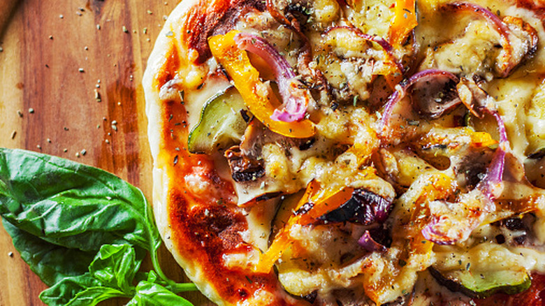 Vegetable pizza on a table with bell peppers, basil, and onions.