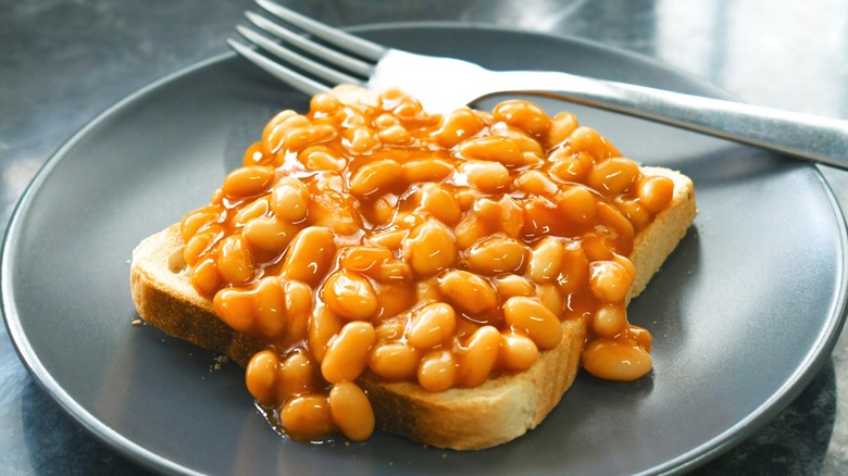 Baked beans on white toast on a black plate with a fork.