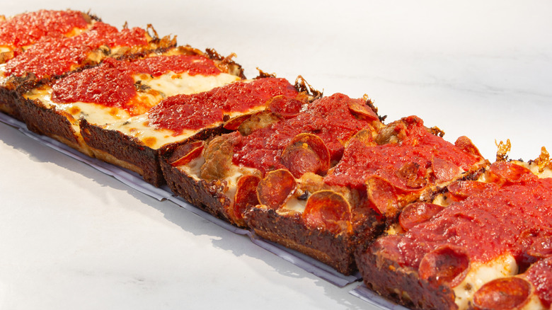 A row of Detroit-style pizza lined up on a countertop.