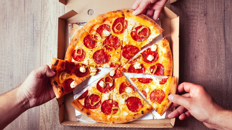 People taking slices of pizza from box