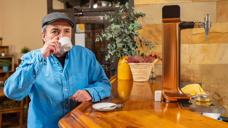 A man standing at an espresso bar, drinking an espresso.