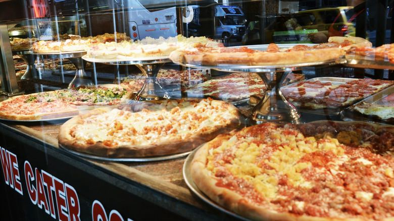 New York pizzas on display in a shop window with buses in the reflection
