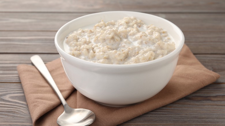A white bowl of oatmeal on a napkin next to a spoon