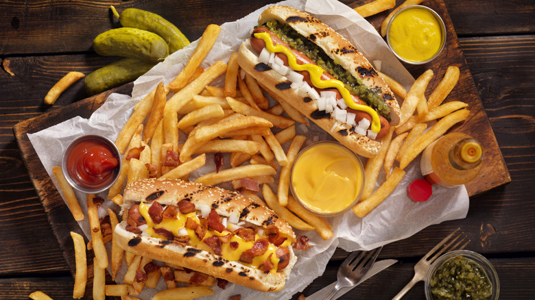 Top view of two hot dogs alongside fries, pickles, ketchup, and mustard