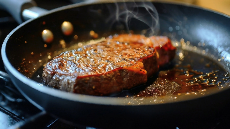 A piece of steak cooking in a black pan on the stove