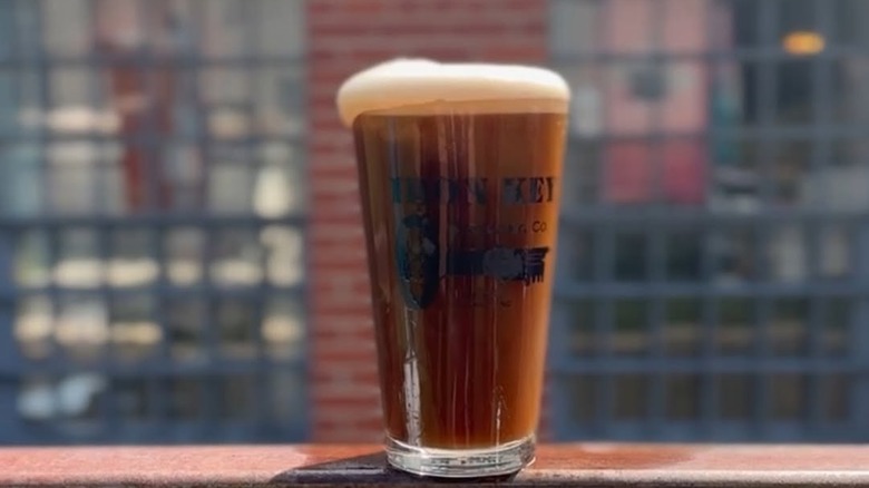 A glass of beer on metal bar in front of Iron Key Brewing