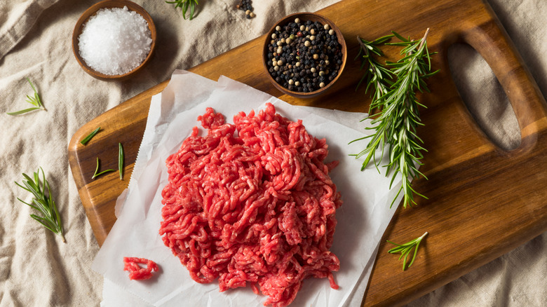 Raw ground beef and seasonings opn a wooden board