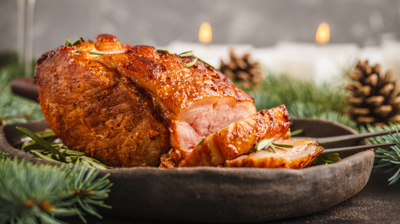 whole baked ham with slices cut from one end surrounded by pine boughs and pine cones