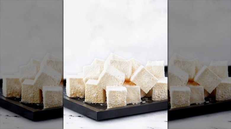 Rustic pile of homemade vanilla marshmallows, coated in powdered sugar. Soft texture, natural shapes. Displayed on black plate with marble background and space for text.