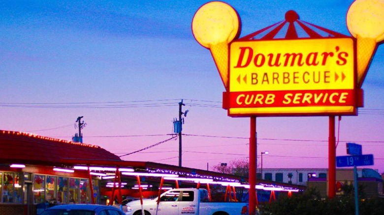 Exterior with lit sigh and cars in curbside parking lot of Doumar´s Barbecue