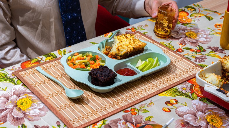 man sitting at a table with a vintage TV dinner arranged in a tray.