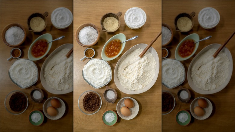 Cookie ingredients consisting of eggs, flour, cocoa, starch, baking powder, baking soda, baking powder, baking soda, cinnamon, jam, placed on wooden kitchen floor. Top shot, with a mise-en-scene.