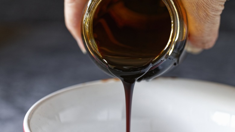 Hand pouring molasses into a white bowl from a jar