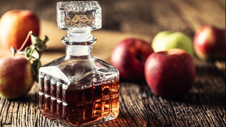 A bottle of apple cider vinegar with fresh apples on rustic wooden table.