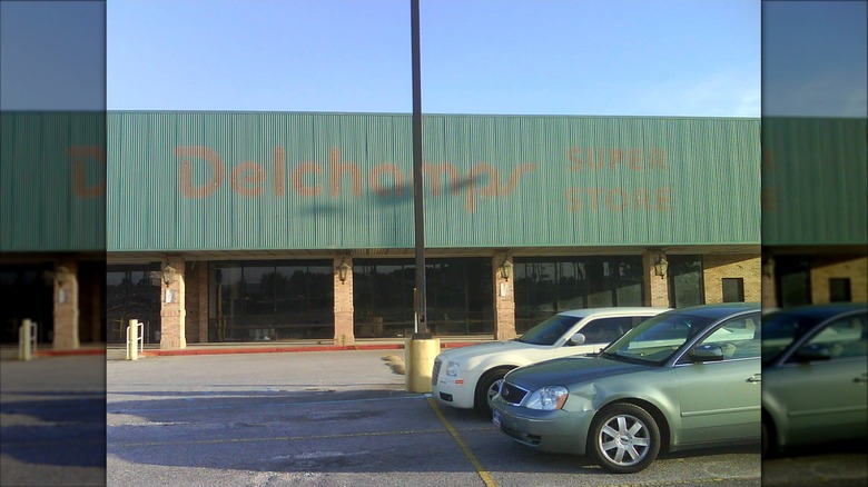 Faded Delchamps signage on green grocery store storefrong near parking lot with two cars