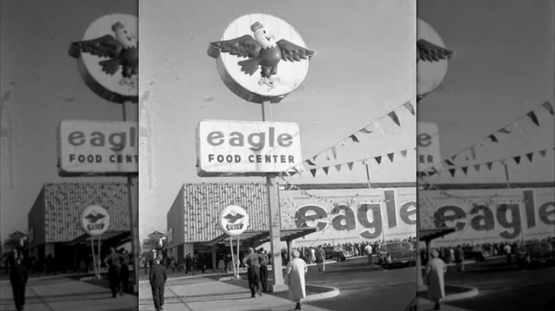 Black and white photo of Eagle Food Center grocery store storefront with several people walking through the parking lot