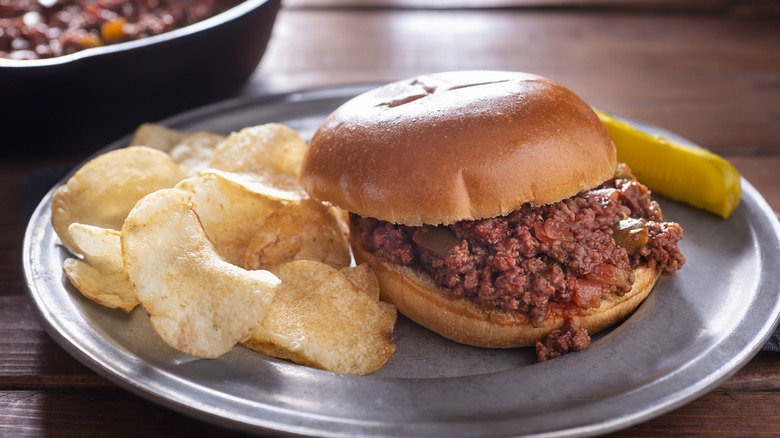 Sloppy Joes on a plate with potato chips and a pickle