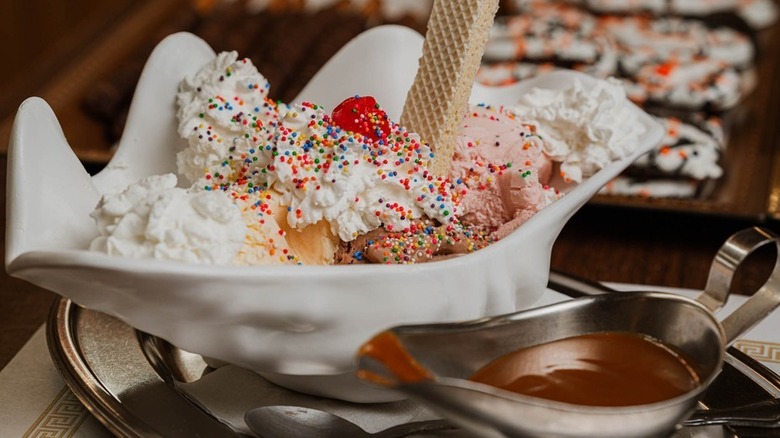Ice cream sundae in a shell bowl with hot fudge on the side