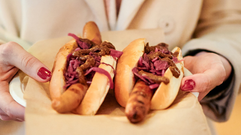 Hands holding tray of dressed hot dogs