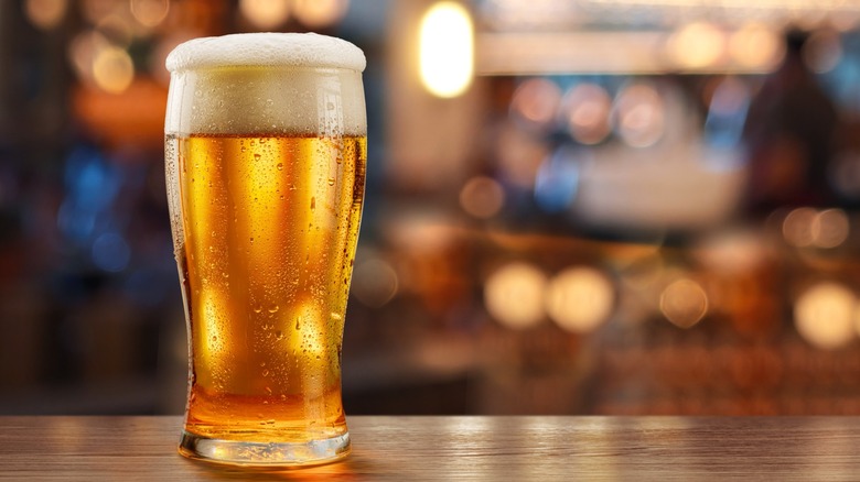 Glass of beer on wooden bar and blurred brightly lit bar interior in the background