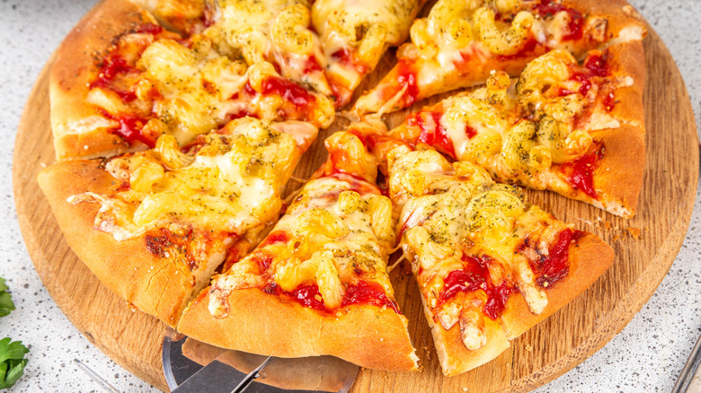 A mac and cheese topped pizza with a metal pizza cutter removing a slice