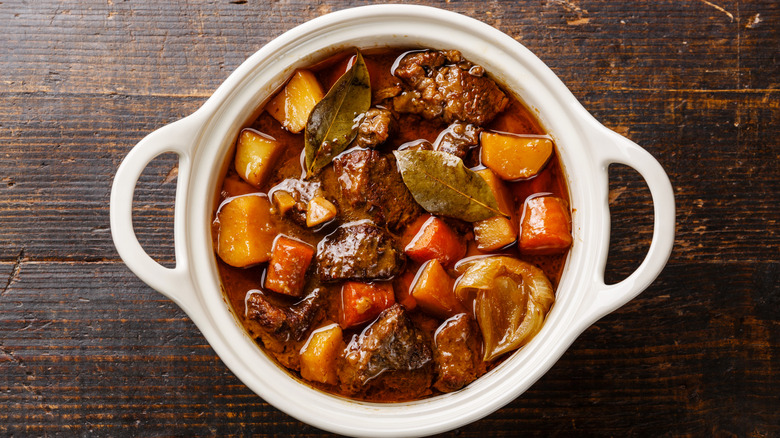 Beef meat stewed with potatoes, carrots and spices in ceramic pot on wooden background