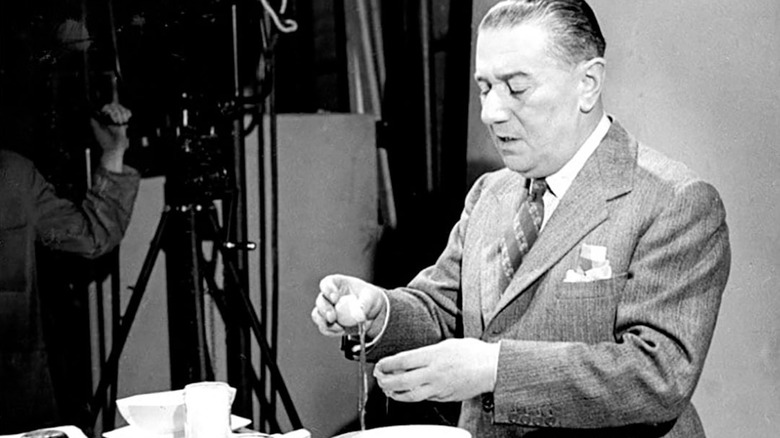 A black and white photo of Xavier Marcel Boulestin being filmed for TV, cracking an egg