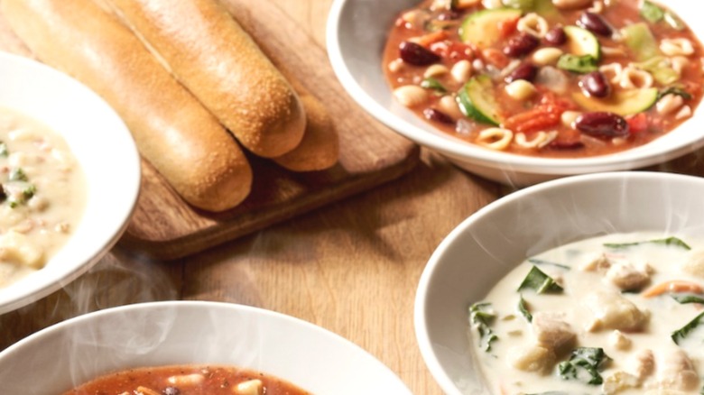 Four soup bowls and multiple breadsticks arranged on a wooden table.