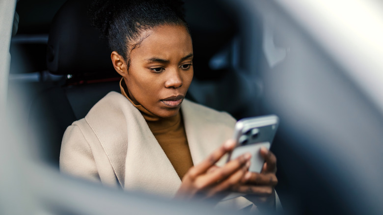 A woman inside a car staring at her phone with a worried look.