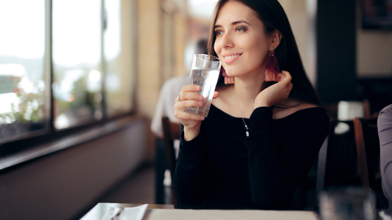 A smiling woman sitting inside a restaurant with a glass of water.
