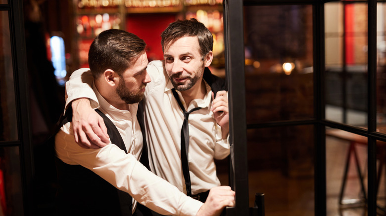 Two men who appear intoxicated leaving a restaurant arm-in-arm.