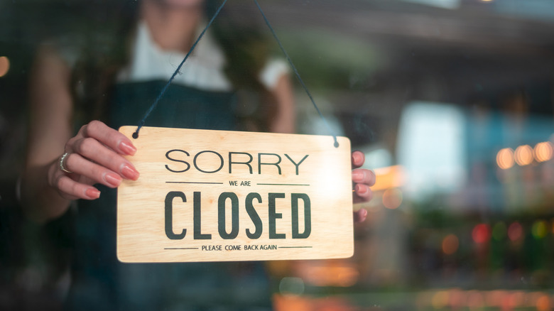 A long-haired woman hanging a closed sign in a restaurant window.