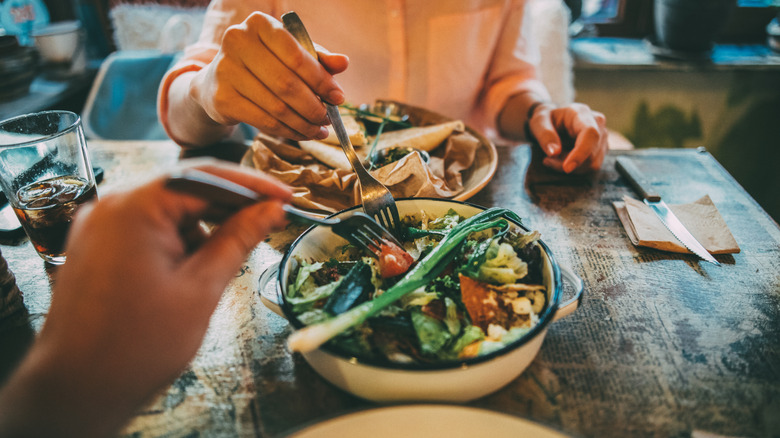 Two people sharing a salad at a restaurant.