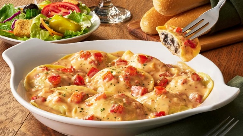 A bowl of ravioli at Olive Garden with a side salad in the background.