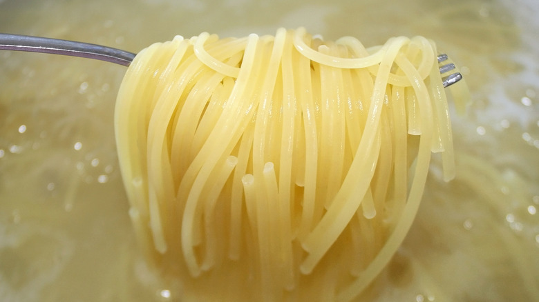 Fork picking up spaghetti cooking in hot water