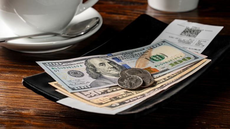 Money on tip tray at restaurant with a coffee mug behind it.