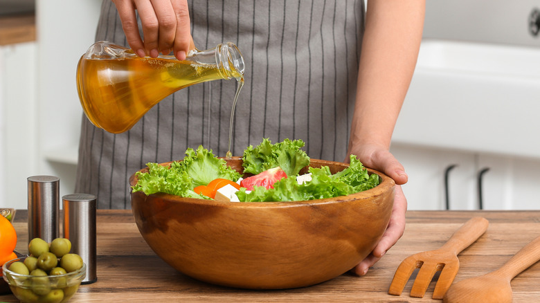 Hands adding dressing to wooden bowl filled with salad