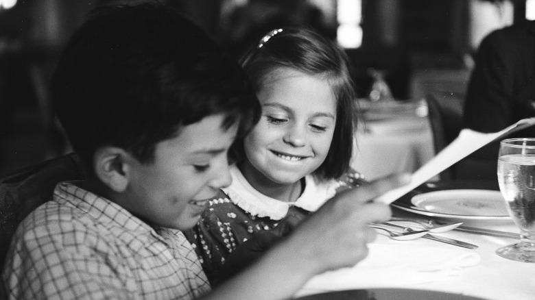 Two children share a laugh as they read lunch menu at a restaurant