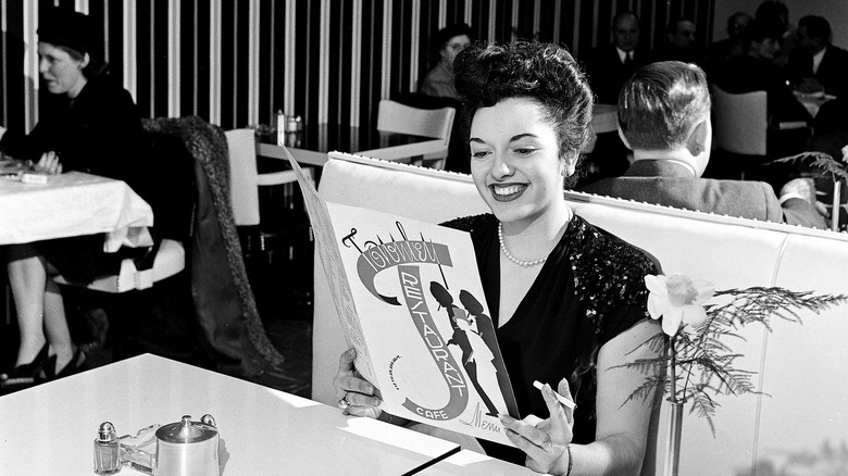 A cigarette in her hand, a woman smiles as she reads the menu