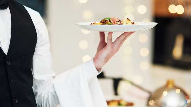 Fine dining, food and waiter serving at a restaurant. Formal, hospitality service and server with a plate or dish for a fancy special dinner date.